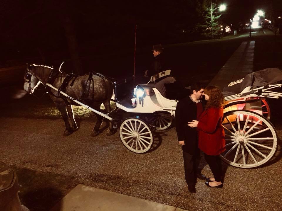 Man and woman hugging in front of horse-drawn carriage